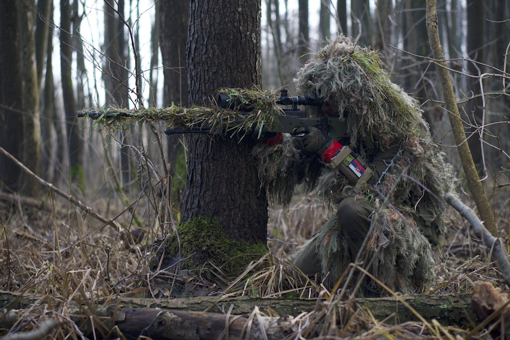 A Soldier Sniper Aiming Though The Rifle Scope In Forest